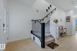 Entryway featuring light wood-finish flooring, a white paneled door with glass insert, and a staircase with black iron balusters and carpeted treads - 
