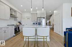 Contemporary kitchen featuring light gray cabinetry, stainless steel appliances, a subway tile backsplash, a central island with countertop seating, and wood-finish flooring - 