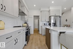 Bright kitchen featuring light-toned cabinetry, stainless steel appliances, a subway tile backsplash, light wood-finish flooring, and a central island with countertop seating - 