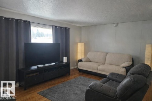Living area featuring wood-finish flooring, a large window with privacy curtains, and a textured ceiling - 13204 131A Avenue Nw, Edmonton, AB - Indoor Photo Showing Living Room