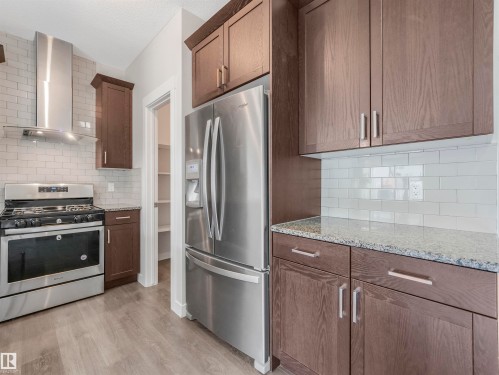 Kitchen featuring stainless steel appliances, dark wood-finish cabinetry, granite countertops, white subway tile backsplash, and wood-finish flooring - 20507 99 Avenue, Edmonton, AB - Indoor Photo Showing Kitchen
