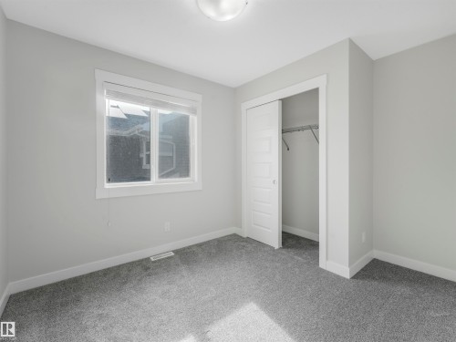 Bright room featuring light gray walls, gray carpeting, a single window with white trim, a built-in closet with sliding panel doors, and a ceiling-mounted light fixture - 20507 99 Avenue, Edmonton, AB - Indoor Photo Showing Other Room