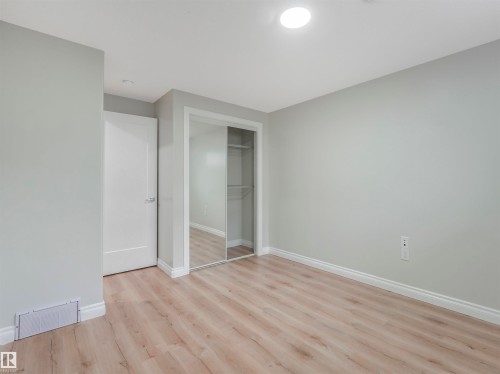 Spacious room featuring light wood-finish flooring, light gray walls, white baseboards, a white interior door, a large mirrored closet, and an overhead recessed light fixture - 20507 99 Avenue, Edmonton, AB - Indoor Photo Showing Other Room