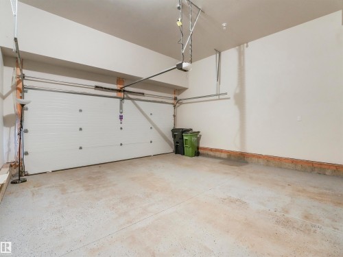 Spacious garage featuring a white sectional door, exposed automatic opener mechanism, painted concrete flooring, and neutral wall finishes - 20507 99 Avenue, Edmonton, AB - Indoor Photo Showing Garage
