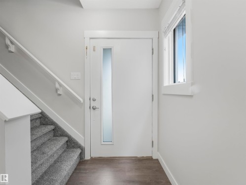 Entryway featuring a white door with a frosted glass insert, wood-finish flooring, a carpeted staircase with white handrail, and a window with white trim - 20507 99 Avenue, Edmonton, AB - Indoor Photo Showing Other Room