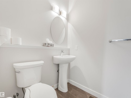 Bathroom featuring a pedestal sink with a chrome faucet, oval wall mirror, and modern vanity lighting - 20507 99 Avenue, Edmonton, AB - Indoor Photo Showing Bathroom