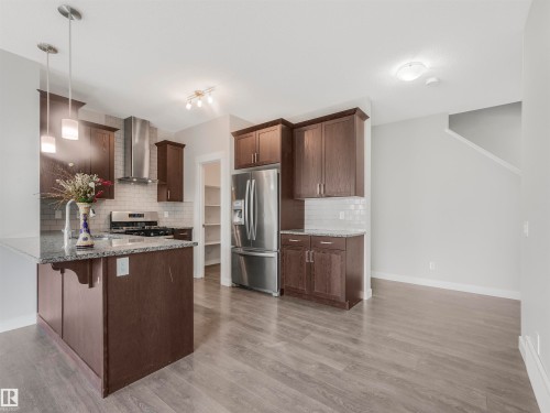 Modern kitchen featuring dark wood cabinetry, stainless steel appliances, an island with a countertop, and wood-finish flooring - 20507 99 Avenue, Edmonton, AB - Indoor Photo Showing Kitchen With Upgraded Kitchen