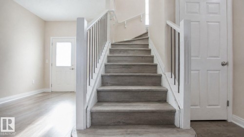 Curved staircase with wood-finish treads and risers, white balusters, and a matching handrail - 8 Meadowlink Common, Spruce Grove, AB 