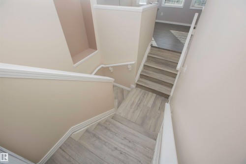 Staircase featuring wood-finish treads and risers, white handrails, and neutral-toned wall paint, complemented by white trim work - 8 Meadowlink Common, Spruce Grove, AB 