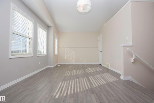 Spacious room featuring light wood-finish flooring, multiple windows with blinds, a white ceiling with a flush-mount light fixture, and a neutral color palette - 8 Meadowlink Common, Spruce Grove, AB 