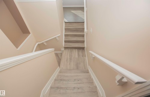 Stairwell with light wood-finish flooring, white baseboards, white handrails, and light neutral wall paint - 8 Meadowlink Common, Spruce Grove, AB 