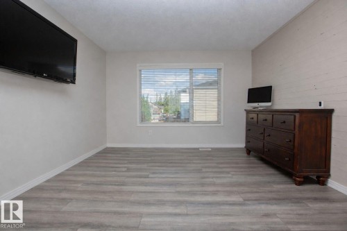 Spacious room featuring wood-finish flooring, a large window with horizontal blinds, and a textured accent wall - 8 Meadowlink Common, Spruce Grove, AB 