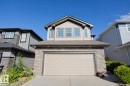 Two-story residential exterior featuring a two-car garage with an overhead door, stacked stone accents, light-toned siding, and multiple upper-level windows - 8 Meadowlink Common, Spruce Grove, AB 