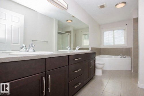 Bathroom featuring a dark wood-finish double vanity with dual sinks, a large mirror, a corner soaking tub, and tile flooring - 8 Meadowlink Common, Spruce Grove, AB 