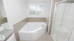 Corner soaking tub with chrome fixtures, complemented by a separate glass-enclosed shower - 