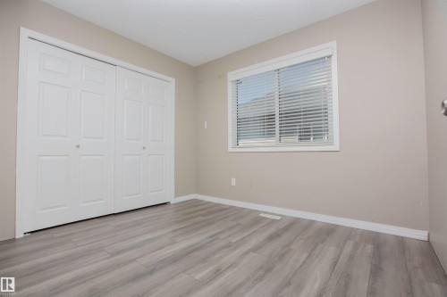 Spacious room featuring light wood-finish flooring, a double bi-fold closet, and a white-trimmed window with horizontal blinds - 8 Meadowlink Common, Spruce Grove, AB 