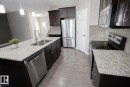 Open-concept kitchen featuring dark wood cabinetry, light speckled countertops, and stainless steel appliances including a refrigerator, dishwasher, and built-in microwave - 8 Meadowlink Common, Spruce Grove, AB 