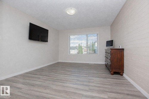 Spacious room featuring wood-finish flooring, a contemporary ceiling light fixture, and a window with horizontal blinds - 8 Meadowlink Common, Spruce Grove, AB - Indoor Photo Showing Other Room
