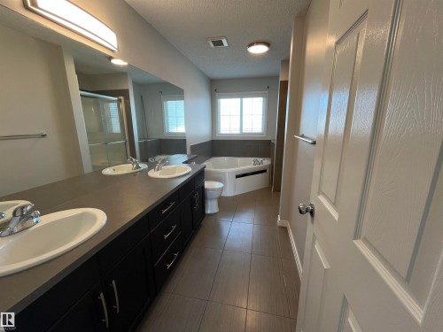 Bathroom featuring a double vanity with dark cabinetry, integrated sinks, and an expansive mirror - 8 Meadowlink Common, Spruce Grove, AB - Indoor Photo Showing Bathroom