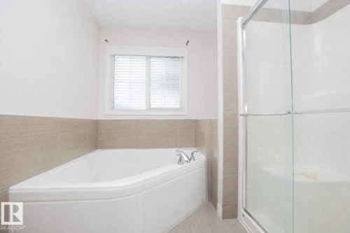Corner soaking tub with chrome fixtures, complemented by a window with blinds, light-toned wall tile, and a glass-enclosed shower - 8 Meadowlink Common, Spruce Grove, AB - Indoor Photo Showing Bathroom