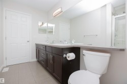 Spacious bathroom featuring a dual-sink vanity with dark wood cabinetry, light-toned countertops, and a full-width mirror - 