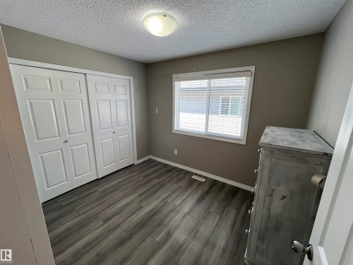 Spacious room featuring wood-finish flooring, a double-door closet, and a large window with white blinds - 8 Meadowlink Common, Spruce Grove, AB - Indoor