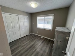 Spacious room featuring wood-finish flooring, a double-door closet, and a large window with white blinds - 