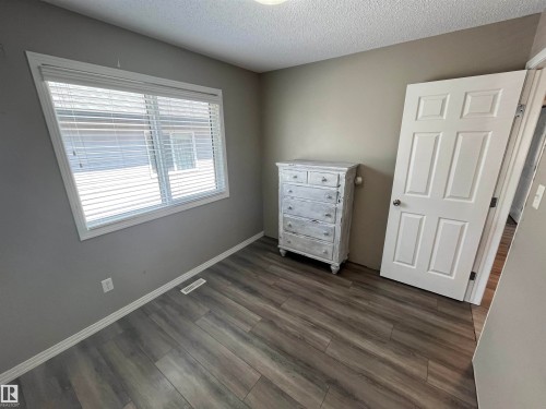 Room featuring wood-finish flooring, a window with blinds, and a paneled door - 8 Meadowlink Common, Spruce Grove, AB - Indoor