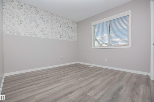 Light gray wood-finish flooring complements soft gray walls and a decorative accent wall featuring a subtle leaf pattern - 8 Meadowlink Common, Spruce Grove, AB - Indoor Photo Showing Other Room