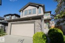 Two-story residential exterior featuring a two-car garage, stone and siding facade, and a covered entry with a light-colored door - 8 Meadowlink Common, Spruce Grove, AB 