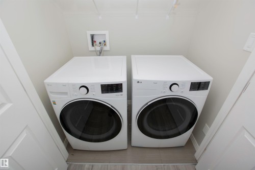 Dedicated laundry space featuring a white front-loading washer and dryer set, neutral wall paint, and light-toned flooring - 8 Meadowlink Common, Spruce Grove, AB - Indoor Photo Showing Laundry Room