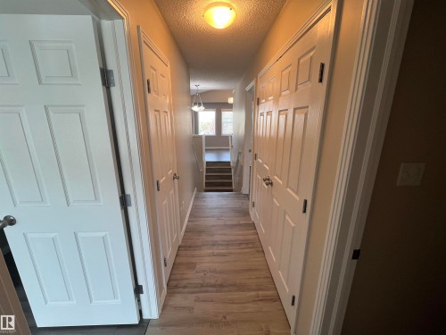 Long hallway featuring wood-finish flooring and multiple paneled doors with chrome hardware - 8 Meadowlink Common, Spruce Grove, AB - Indoor Photo Showing Other Room