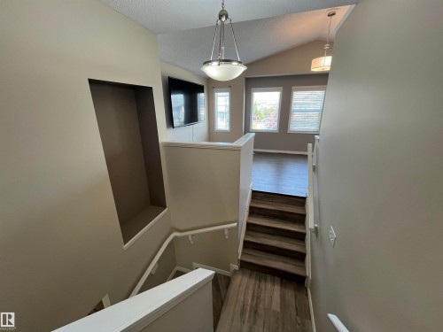 Staircase with wood-finish treads and white risers, leading to a living area with vaulted ceilings - 8 Meadowlink Common, Spruce Grove, AB - Indoor Photo Showing Other Room