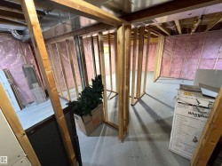Unfinished basement area featuring framed wall structures, exposed insulation, open ceiling joists, and concrete flooring - 