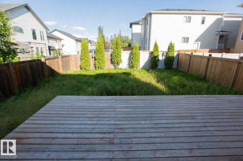Expansive backyard featuring a wood deck, natural grass, perimeter wood fencing, and mature evergreen plantings - 8 Meadowlink Common, Spruce Grove, AB - Outdoor With Exterior