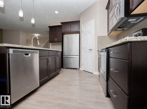 Kitchen featuring dark wood cabinetry, light granite countertops, and stainless steel appliances - 8 Meadowlink Common, Spruce Grove, AB 