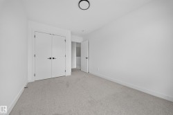 Neutral-toned carpeted room featuring a double-door closet with matte black hardware, white baseboards, and a contemporary ceiling light fixture - 