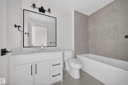 Contemporary bathroom featuring a white vanity with a single basin sink, matte black hardware, and a framed mirror - 