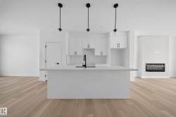 Open-concept living space featuring a central kitchen island with a built-in sink and three pendant lights - 