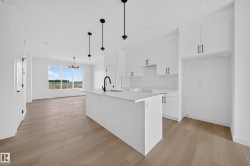 Open-concept kitchen featuring white shaker cabinetry, an island with an undermount sink, a matte black gooseneck faucet, light wood-finish flooring, and pendant lighting - 