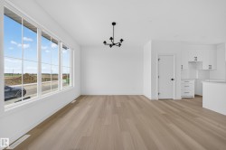Open-concept living space with expansive multi-pane windows, wood-finish flooring, a contemporary black chandelier, and white walls - 
