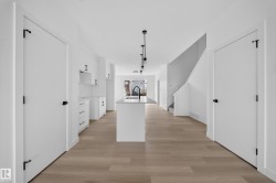 Open-concept kitchen and living area featuring a central island with a sink, pendant lighting, wood-finish flooring, and white cabinetry - 