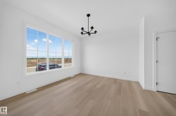 Spacious room featuring a large multi-pane window, wood-finish flooring, a contemporary black chandelier, white walls, and white baseboards - 