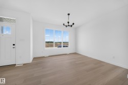 Open concept living area featuring light wood-finish flooring, a contemporary black chandelier, and a white paneled entry door with clear glass inserts - 