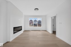 Bright living space featuring a built-in electric fireplace, recessed wall-mounted media connections, wood-finish flooring, a contemporary flush-mount ceiling light, and white trim throughout - 