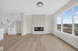 Spacious living area featuring light wood-finish flooring, a contemporary fireplace, and a wall of three large windows - 