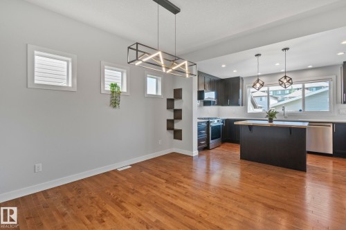 Open-concept living space featuring wood-finish flooring, a modern linear chandelier, and contemporary wall shelving - 614 Mcdonough Link, Edmonton, AB 