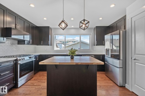 Kitchen featuring dark cabinetry, stainless steel appliances, a center island with a wood-finish countertop, white subway tile backsplash, and recessed lighting - 614 Mcdonough Link, Edmonton, AB 