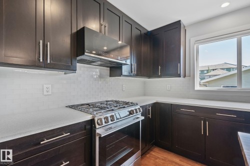 Kitchen featuring dark wood cabinetry, light countertops, a stainless steel range, a subway tile backsplash, and a window - 614 Mcdonough Link, Edmonton, AB 