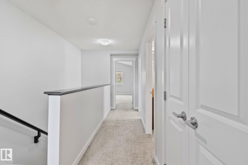 Upper-level hallway featuring neutral carpeting, white paneled doors with brushed nickel hardware, and a white and black stair railing - 614 Mcdonough Link, Edmonton, AB 